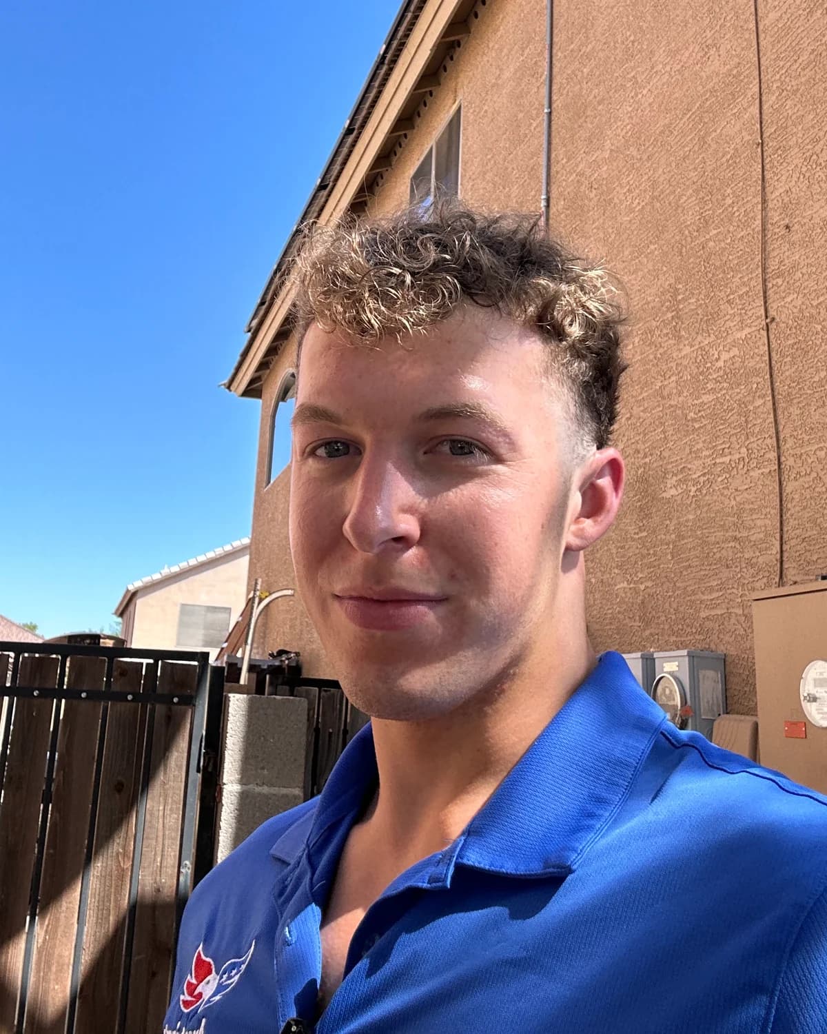 Hayden Mitchell at a homeowner estimate in Arizona in 2023, wearing a blue company polo between two stucco homes in bright daylight.
